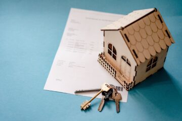 A small wooden house on top of a piece of paper, keys next to it.